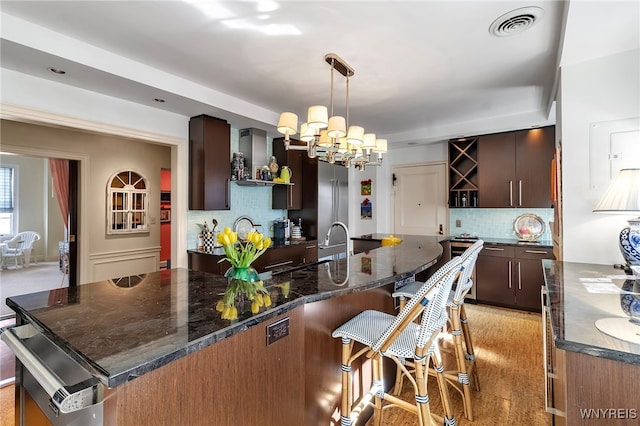 kitchen featuring tasteful backsplash, visible vents, decorative light fixtures, a kitchen bar, and a sink