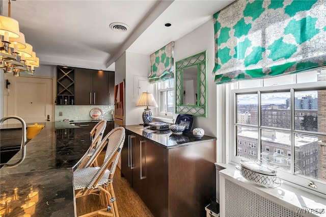 kitchen with tasteful backsplash, radiator heating unit, plenty of natural light, and visible vents