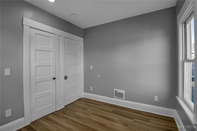 unfurnished bedroom with a closet, dark wood-style flooring, visible vents, and baseboards