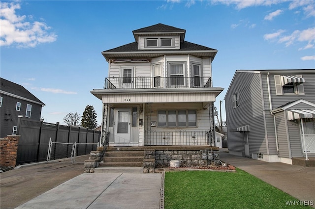 american foursquare style home with a balcony, roof with shingles, a gate, fence, and a porch