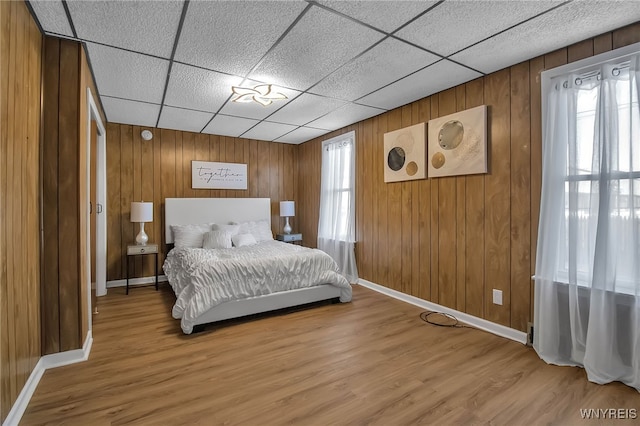 bedroom featuring a drop ceiling, multiple windows, and light wood-type flooring