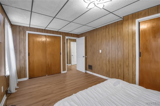 bedroom featuring a closet, a drop ceiling, wooden walls, and wood finished floors