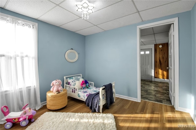 bedroom featuring a drop ceiling, baseboards, and wood finished floors