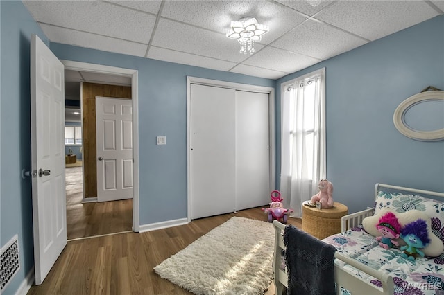 bedroom with baseboards, visible vents, a drop ceiling, wood finished floors, and a closet