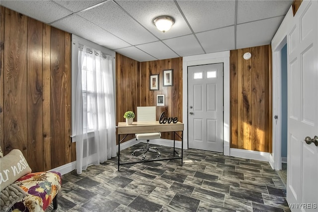 home office with a paneled ceiling, wooden walls, and baseboards