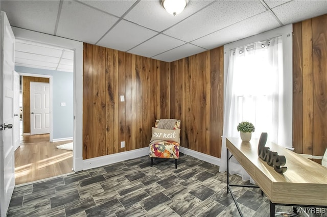 sitting room with a paneled ceiling, wood walls, and baseboards