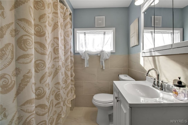 full bath with toilet, vanity, visible vents, and tile walls