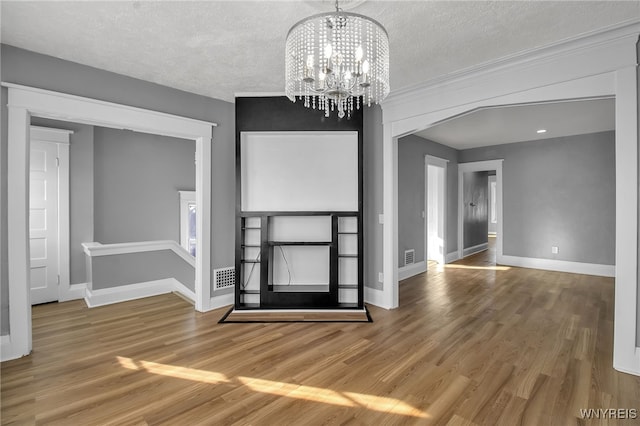 interior space featuring baseboards, arched walkways, wood finished floors, an inviting chandelier, and a textured ceiling