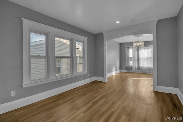 spare room with an inviting chandelier, wood finished floors, and baseboards