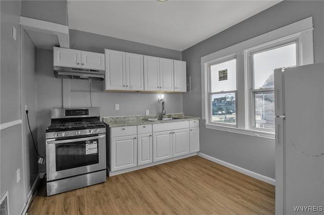 kitchen with stainless steel gas stove, white cabinets, freestanding refrigerator, under cabinet range hood, and a sink