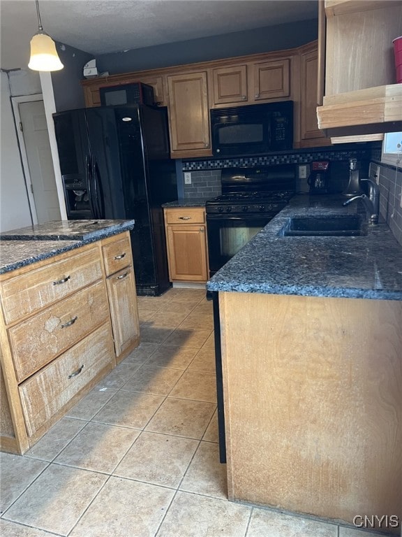 kitchen featuring light tile patterned floors, a sink, backsplash, dark stone counters, and black appliances