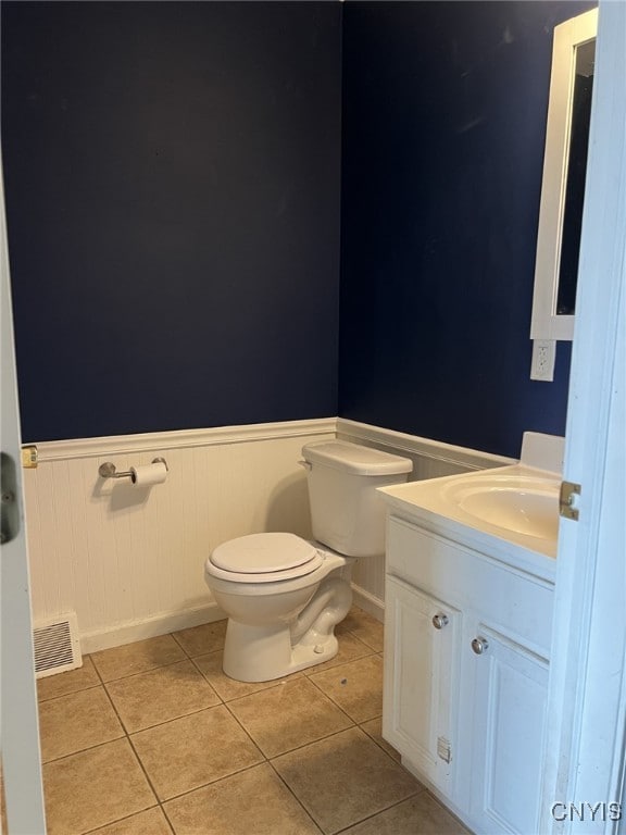 half bathroom with visible vents, toilet, wainscoting, vanity, and tile patterned floors