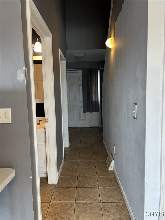 corridor featuring a sink, baseboards, and light tile patterned floors