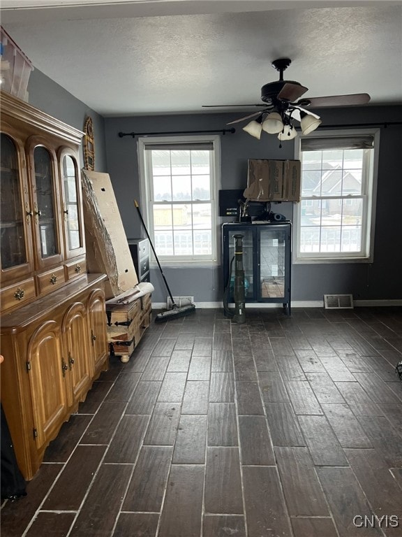 unfurnished living room with a textured ceiling, ceiling fan, visible vents, baseboards, and wood tiled floor