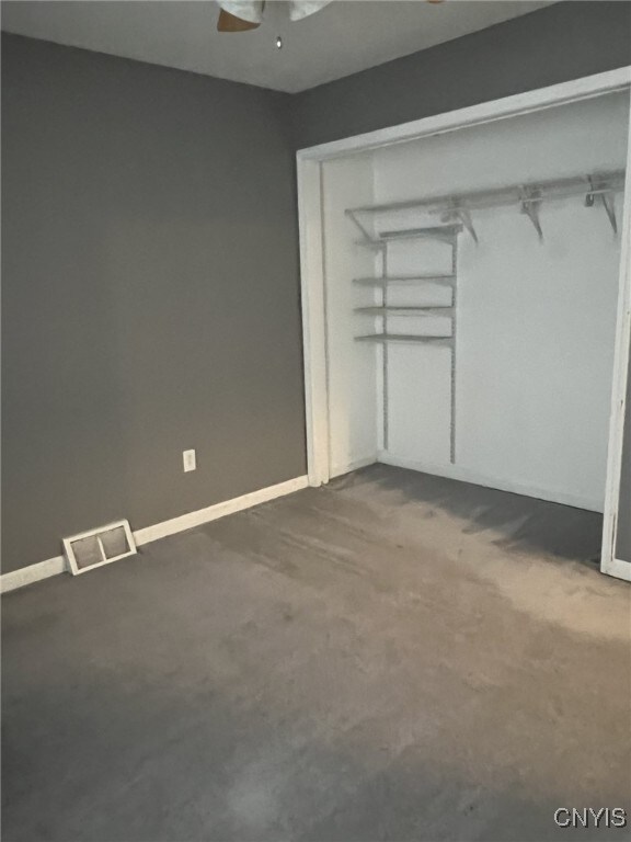 unfurnished bedroom featuring baseboards, dark colored carpet, visible vents, and a ceiling fan