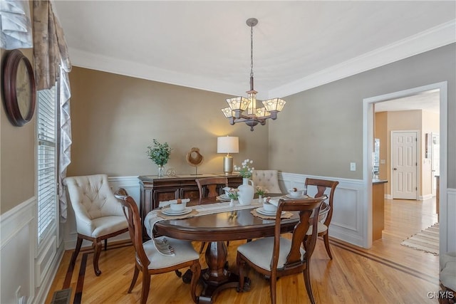 dining space with a chandelier, wainscoting, ornamental molding, and light wood-style flooring