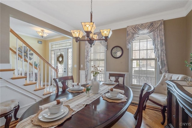 dining space with wood finished floors, stairs, ornamental molding, wainscoting, and an inviting chandelier