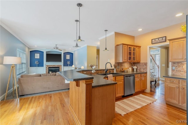 kitchen with dark countertops, a peninsula, a healthy amount of sunlight, stainless steel dishwasher, and a sink