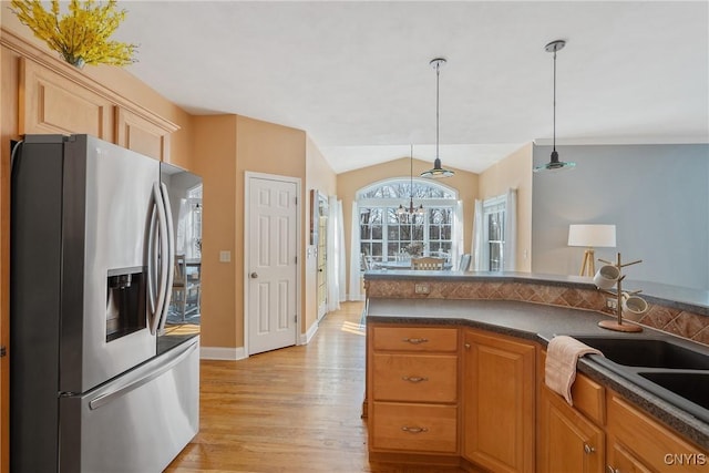 kitchen featuring vaulted ceiling, hanging light fixtures, stainless steel refrigerator with ice dispenser, light wood finished floors, and dark countertops