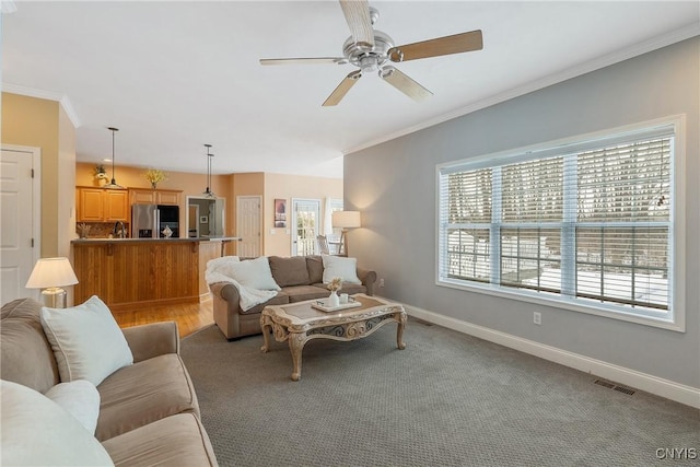 living room with ornamental molding, a ceiling fan, visible vents, and baseboards