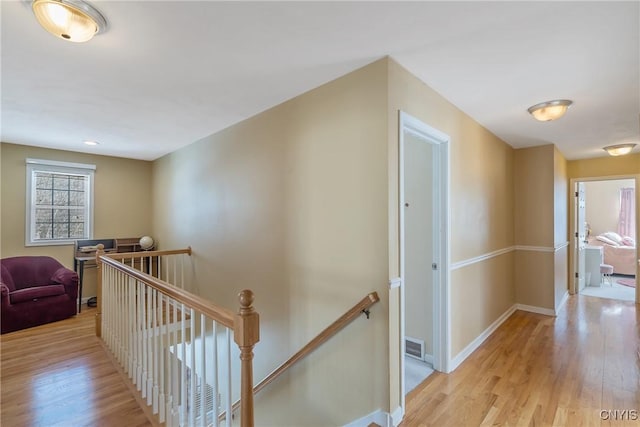 hallway with visible vents, baseboards, an upstairs landing, and light wood-style floors