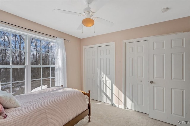 bedroom with light carpet, ceiling fan, and two closets