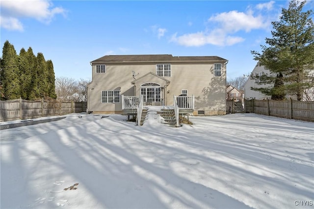 snow covered back of property with a fenced backyard and a wooden deck