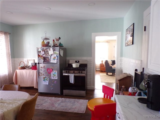 kitchen featuring a wainscoted wall, tile walls, stainless steel appliances, and wood finished floors