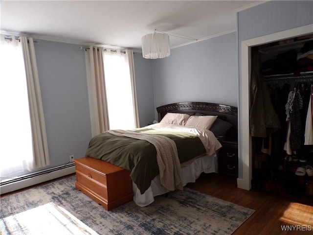 bedroom with ornamental molding, a closet, baseboard heating, and wood finished floors