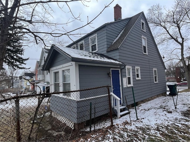 snow covered property featuring roof with shingles, fence, and a chimney