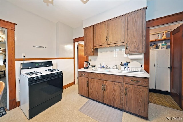 kitchen featuring light countertops, backsplash, a sink, and range with gas stovetop