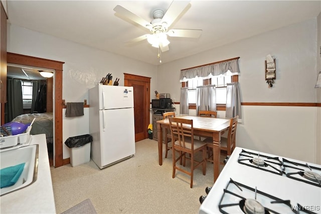 kitchen featuring tile countertops, ceiling fan, freestanding refrigerator, black microwave, and a sink