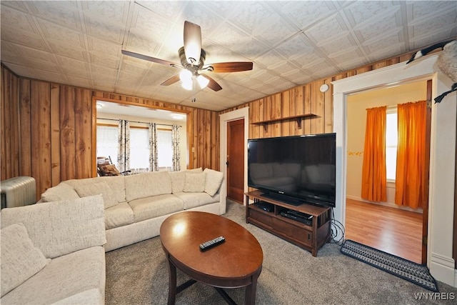 carpeted living area featuring an ornate ceiling, wooden walls, and a ceiling fan