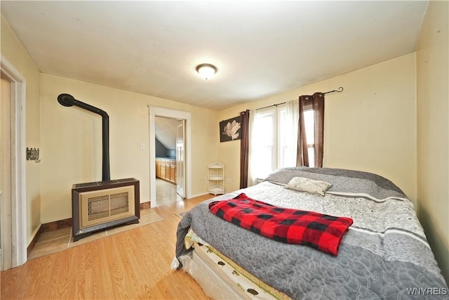 bedroom featuring a wood stove, connected bathroom, and wood finished floors