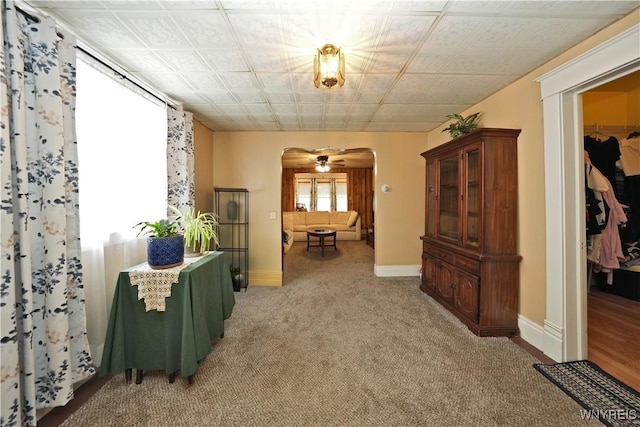 corridor featuring baseboards, arched walkways, and light colored carpet