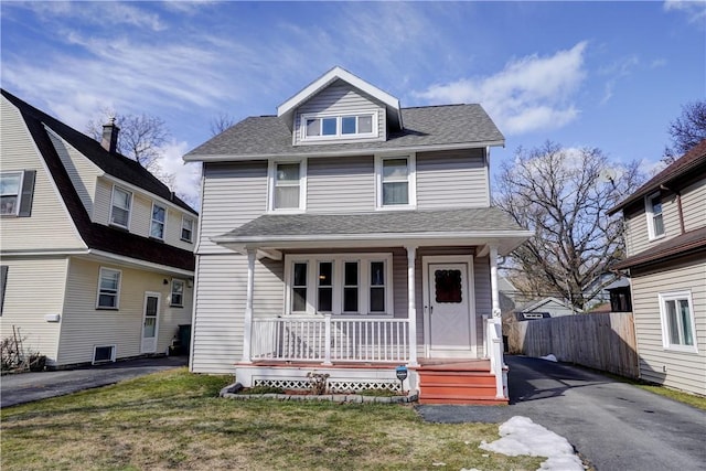 american foursquare style home with covered porch, a shingled roof, fence, and a front yard