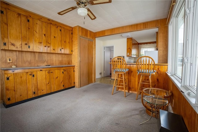 interior space featuring light colored carpet, wood walls, and ceiling fan