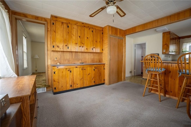 kitchen with carpet floors, brown cabinets, and wood walls