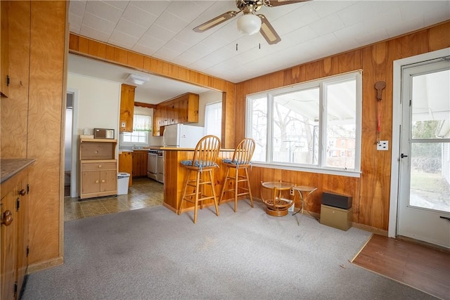 kitchen featuring brown cabinetry, freestanding refrigerator, dark carpet, and wooden walls