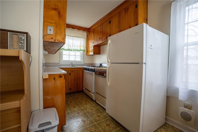 kitchen featuring dark floors, white appliances, a sink, light countertops, and brown cabinets