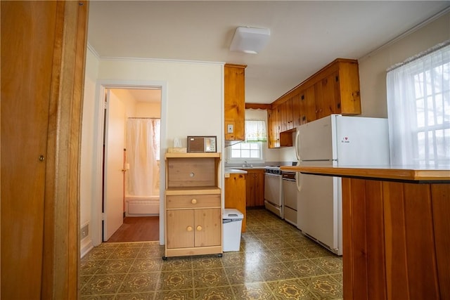 kitchen with dark floors, brown cabinets, freestanding refrigerator, crown molding, and a sink