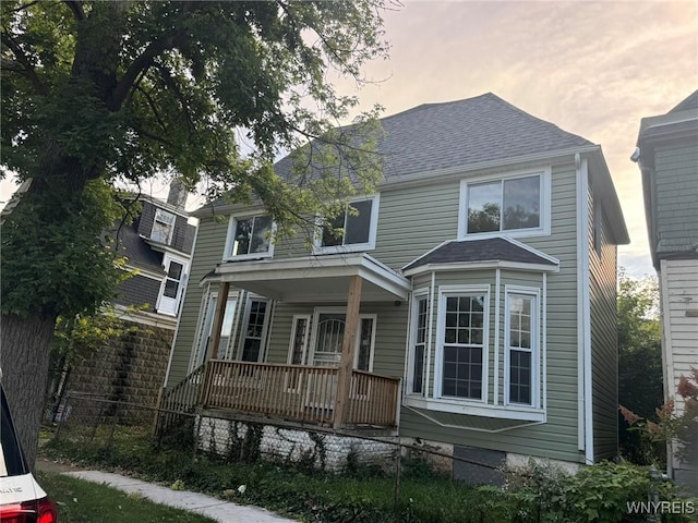 american foursquare style home featuring a shingled roof, fence, and a porch