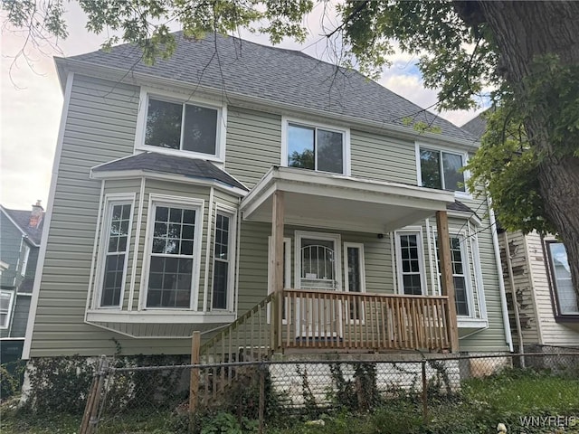 american foursquare style home with covered porch, a fenced front yard, and roof with shingles