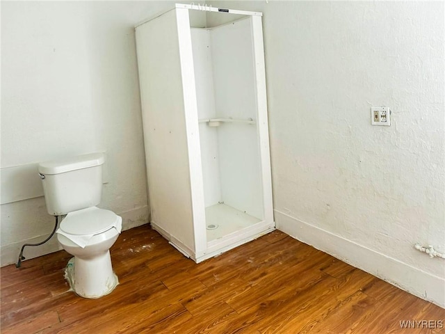 full bath featuring toilet, a stall shower, and wood finished floors