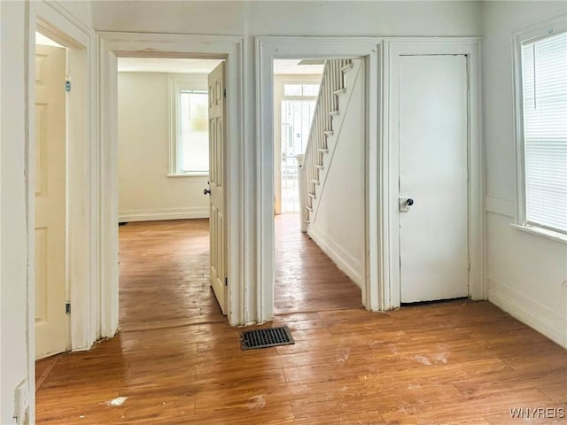 hallway featuring light wood-type flooring, stairway, baseboards, and visible vents