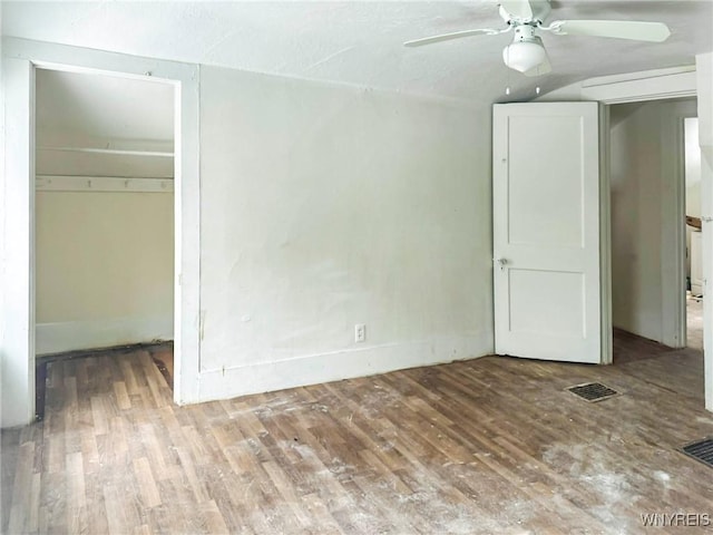 unfurnished bedroom featuring a spacious closet, wood finished floors, visible vents, and a ceiling fan