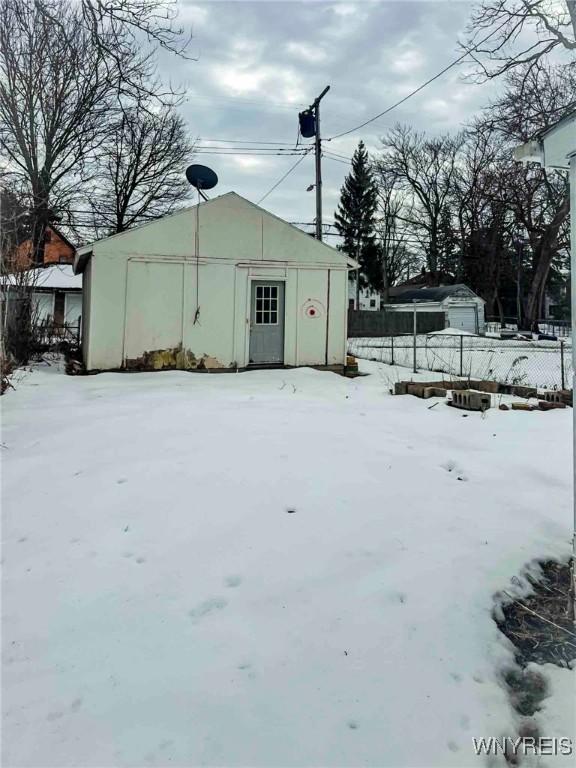 snow covered structure featuring fence and an outbuilding