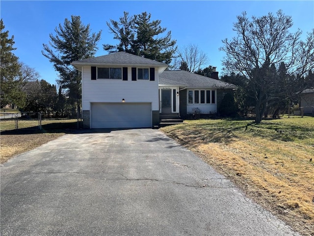 split level home with an attached garage, a chimney, driveway, and fence