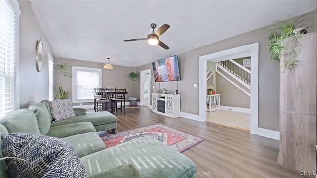 living area with ceiling fan, stairway, baseboards, and wood finished floors