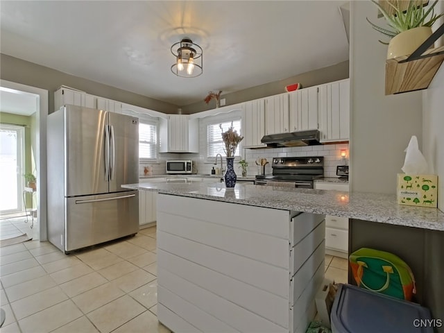 kitchen with under cabinet range hood, tasteful backsplash, light tile patterned floors, and stainless steel appliances